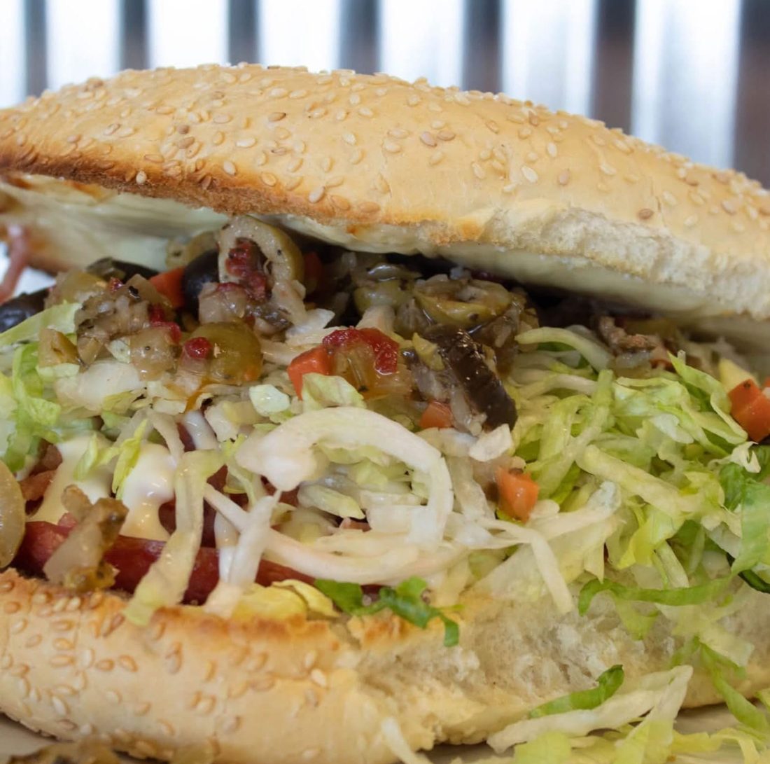 A loaded muff on a sesame roll, piled with olive salad and shredded lettuce